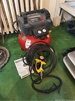 Front view of red Porter-Cable air compressor with control panel, pressure gauges, and attached hose with yellow nozzle laid out in front along with an instruction manual.