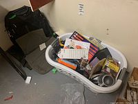 Laundry basket filled with various items including Mastercraft cordless screwdriver kit, ceramic mug, power bar, and assorted desk and game accessories.