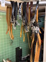Photo showing various leather belts hanging on a rod with brown and black colors and plastic-wrapped buckles