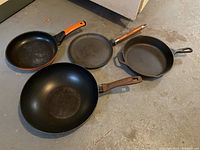 Four pans on ground showing variety including cast iron skillets and wok