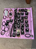 Lot of various costume jewelry including earrings on branded cards, bracelets, and necklaces laid out on pink cloth.