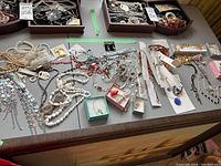 Overview of assorted costume jewellery including necklaces, bracelets, brooches displayed on a table, some pieces in original packaging and small boxes.