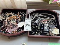 Two wooden drawer trays each containing multiple necklaces and bracelets in varied styles and colors, with visible tags on some pieces