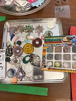 Photo of a metal tray holding various stone charms, costume jewelry rings, star-shaped translucent pendants, a flower accessory, and geometric pendants. Includes boxed set of stone charms.
