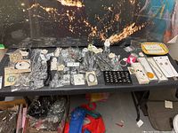 Wide view of a table with costume jewellery items spread out showing necklaces, rings, bracelets mostly in packaging and clear plastic bags