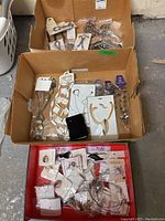 Photo of three boxes containing assorted costume jewellery including necklaces, charms, and earrings in mostly original packaging.