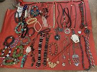 Overhead view of assortment of costume jewelry on red cloth showing bracelets and necklaces with various colors and styles