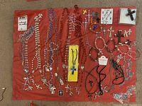 Full spread of costume jewelry laid out on red fabric showing multiple beaded necklaces, bracelets, cross charms, and earrings.