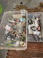 Plastic containers filled with assorted costume jewelry including rings, bracelets, and mixed jewelry pieces in bags