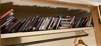Shelf with a large assortment of DVD cases, some stacked and some upright in shelves in a basement or storage area.