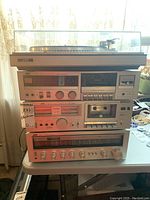 Full view of stacked JVC stereo system including turntable, two cassette decks, and receiver on table with clear dust cover on turntable.