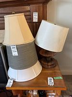 Wooden lamp with turned wood base and four fabric lamp shades stacked beside it on a small wooden table.