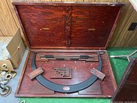 Open wooden case showing micrometer frame, extension rods and accessories