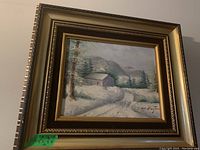 Front view of the framed landscape painting showing the winter cabin scene and signature