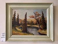 Frontal view of the framed painting depicting a riverside landscape with pine trees and a colorful deciduous tree during autumn.