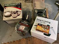 Lot overview photo showing all items: Lagostina pot in packaging, Arcosteel mixing bowls box, chafing stand, fabric steamer box, and magnetic poetry kit.