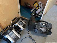 Two Eliminator battery booster packs with air compressors, APC UPS, Eliminator PowerBox and assorted power strips on basement floor
