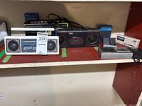 Shelf with radios including white Suntone stereo AM/FM radio, black and red Time stereo cassette deck, handheld radios, and guitar tuner