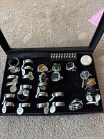 Top view of 22 rings in a black display tray, showing various metal and gemstone rings with size tags 22, 18, and 17.