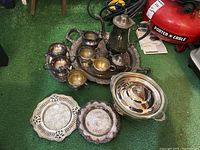 Image showing a group of silver plated items including a teapot, creamers, sugar containers, and serving trays on green surface.