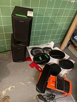 Sony bookshelf speakers stacked with Pioneer car speakers, Soundwave Bluetooth speaker, Sony NAV-U GPS device on floor with green tile background