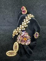 Five piece lot including filigree ring with purple stone, Nolan Miller pansy brooch with purple stones, gold tone bracelet, and two pairs of earrings.