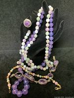 Set of five pieces shown on a black display hand and surface, includes necklaces, bracelets, and ring.