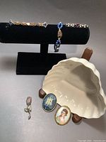 Full view of all 7 pieces including bracelet, bar brooches, porcelain brooch, cameos, rose brooch, and Belleek dish on display stand.