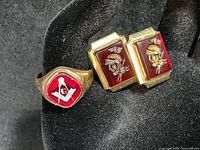 Two-piece lot shown on display with a dark pink/red Masonic ring and a pair of carved red stone intaglio cuff links with Roman soldier designs.