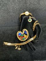 Gold tone Napier bracelet, multicolor artist palette brooch, Mickey Mouse watch, Figaro chain with pendant, and post earrings displayed on black hand stand showing full lot