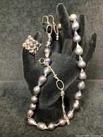 Four-piece black pearl jewelry set displayed on black hand model, including necklace, bracelet, earrings, and ring.