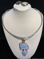 Front view of sterling silver collar necklace with polished stone pendant, silver and gold earrings, and silver ring displayed on white bust stand.
