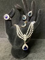 Five-piece blue crystal costume jewelry set displayed on black mannequin hand showing necklace, ring, and two earrings.