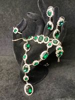 Jewelry pieces displayed on black hand form to show scale and design: necklace, bracelet, earrings, ring with green stones and clear rhinestone surrounds.