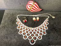 Four pieces displayed on black felt: rhinestone collar, ring, earrings, and heart-shaped glass box.