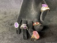 5 costume cocktail rings displayed on black jewelry hand, showing pink, purple, and clear stones with gold and silver tone metals.