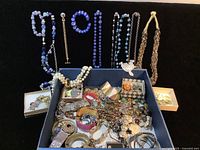 Overview of box filled with assorted costume jewelry including necklaces, bracelets, brooches, earrings and rings