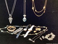 Photo showing most of the jewelry lot including two watches, multiple necklaces, bracelets, and earrings spread on black background