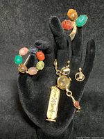 Five pieces displayed on black hand stand: cartouche pendant, watch, earrings, two brooches