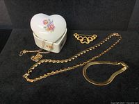 All the gold-tone jewelry pieces alongside the ceramic heart-shaped trinket box with floral lid design, showing the variety of shapes and styles.