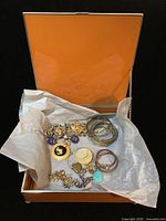 Photo of orange square glass jewelry box open showing tissue paper inside with assorted costume jewelry pieces.