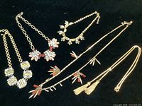 Full view of the 5 J. Crew brass and gold-tone necklaces arranged from left to right on a black surface, showing pendants and designs.