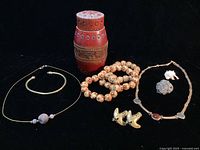 Overview of all 10 items arranged on black background. Includes necklaces, bracelet, earrings, wooden jar, pyrite, and camel pendant.