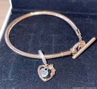 Full view of the rose gold plated snake chain bracelet with T-bar clasp and attached heart and rose flower charm.