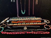 Overview of polished stone costume jewelry including necklaces and bracelets laid flat showing color and styles.