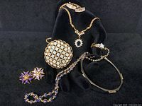 Full lot arranged on black display hand and flat surface showing all seven pieces: gold necklaces, engagement ring, Trifari rhinestone brooch, two pairs of earrings, and bangle bracelet.