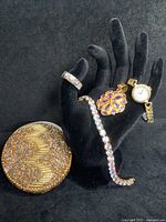 Five jewelry pieces displayed on black velvet hand stand and surface, showing the ring, bracelet, pendant, watch, and beaded box.