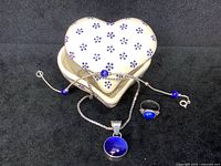 Four items displayed: heart-shaped pottery dish, blue cats eye bracelet, blue cats eye ring, and pendant on silver-tone chain.