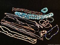 Full collection of over 10 stone bead necklaces and bracelets arranged on black background showing variety of colors and styles.