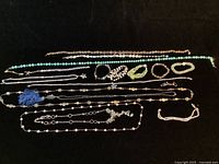 Full view of all jewelry pieces laid out on black background including necklaces and bracelets in varying colors and styles.